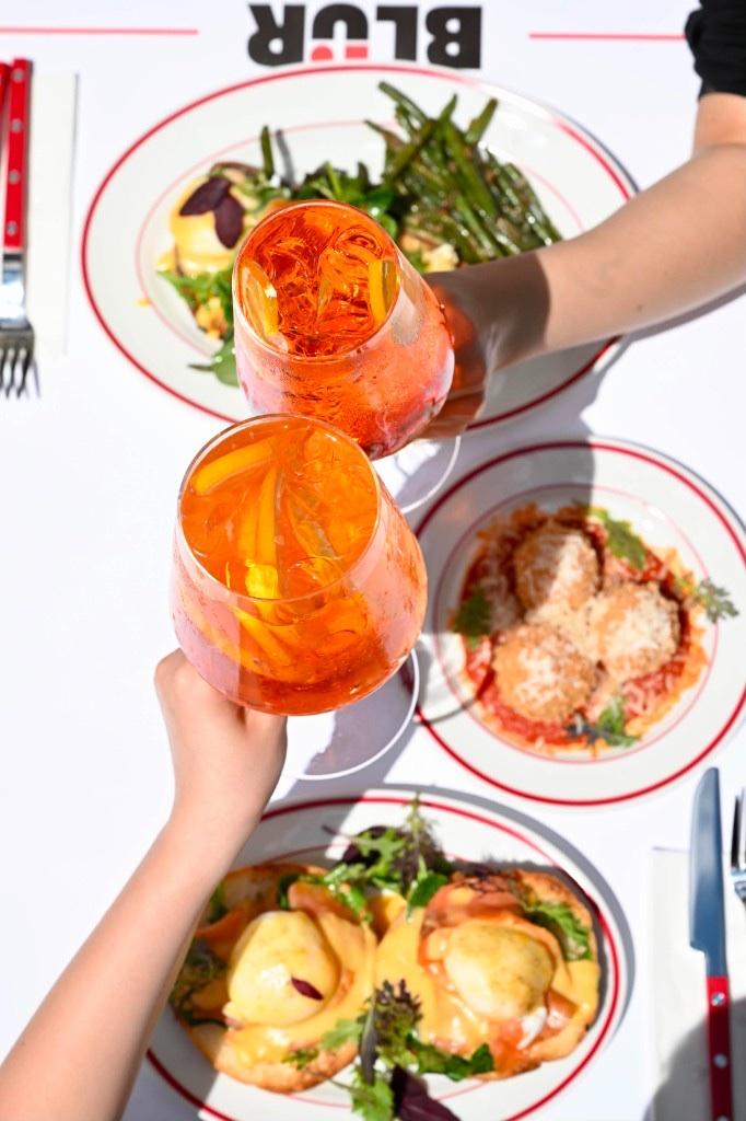 Două mâini ciocnind pahare de spritz deasupra mesei pline