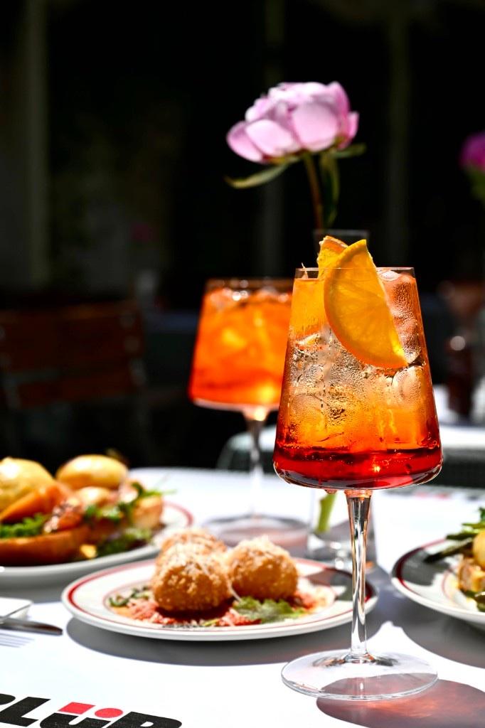 Două pahare de spritz în lumina serii, cu un bujor în fundal