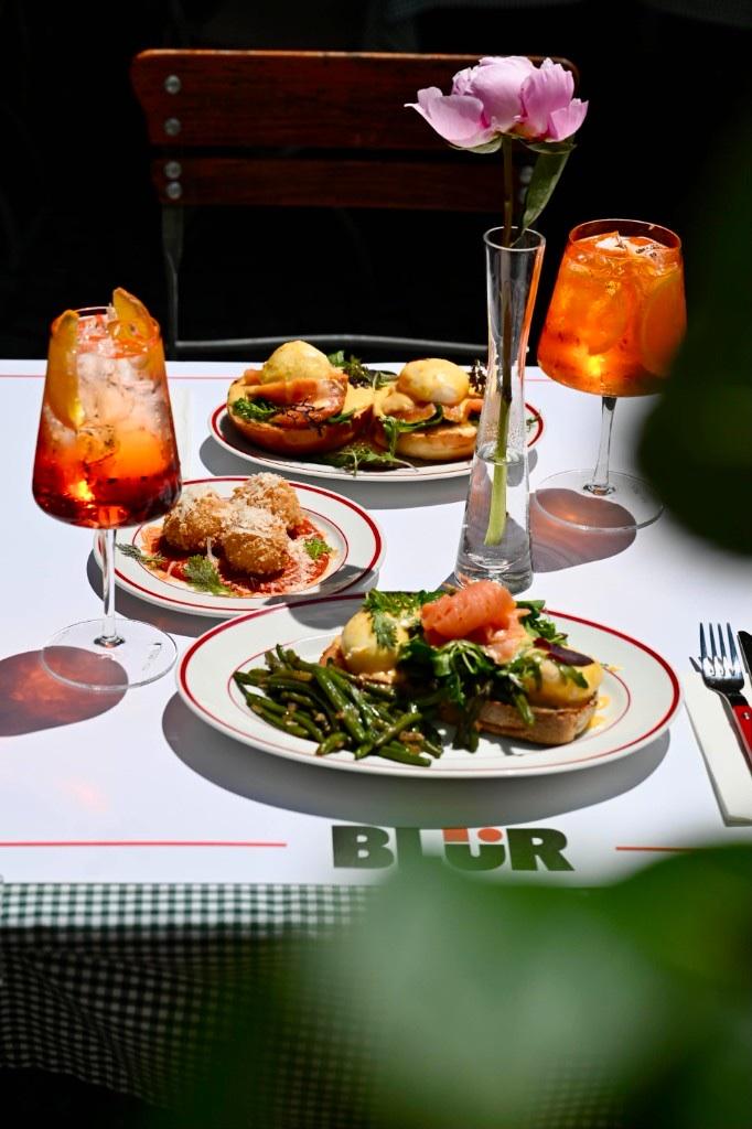Masă pe terasa BLÜR — spritz, brunch și bujori, cu logo-ul BLÜR pe față de masă